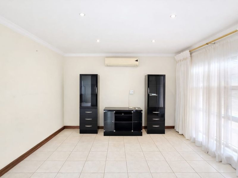 A bright and spacious living area featuring neutral ceramic floor tiles, recessed downlighting, and a wall-mounted air conditioning unit.