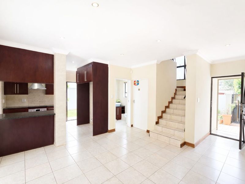 Open-plan living area featuring a kitchen with dark wood cabinetry, granite countertops, and a tiled staircase leading to the upper level.