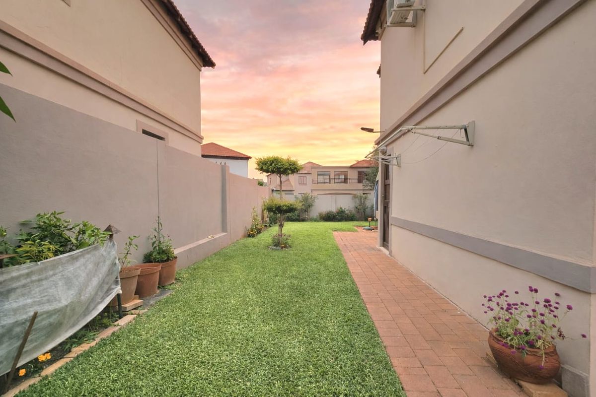 A well-maintained rear garden featuring a neat lawn, paved pathway, and boundary walls, providing a private outdoor space.