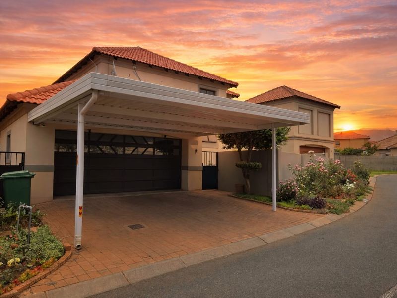 Front exterior view of a residential property featuring a paved driveway, a covered carport, and a secure garage entrance at sunset.