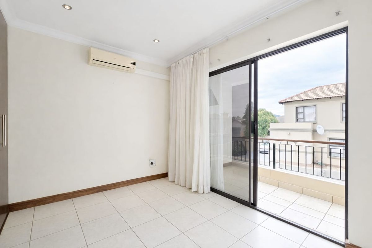 A bright, empty bedroom featuring tiled floors, a built-in air conditioning unit, and sliding glass doors that open onto a private balcony.
