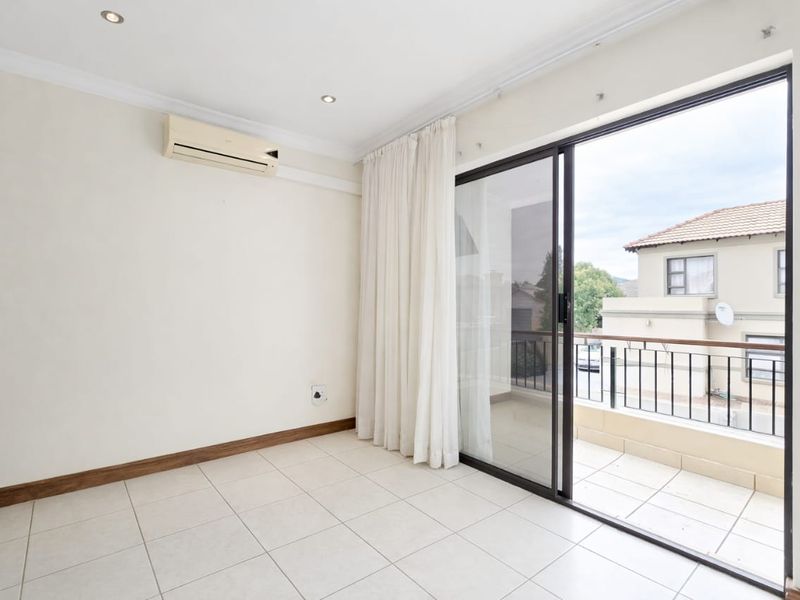 A bright, empty bedroom featuring tiled floors, a built-in air conditioning unit, and sliding glass doors that open onto a private balcony.