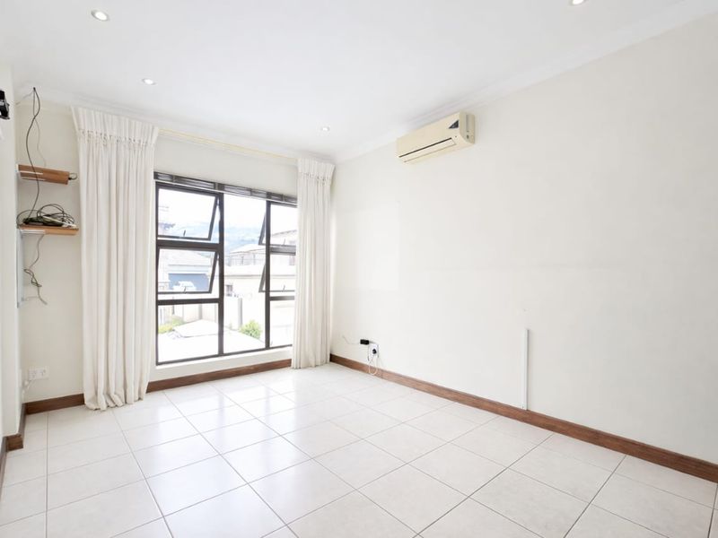 A bright, empty living room featuring tiled flooring, recessed downlights, and a wall-mounted air conditioning unit with large windows providing natural light.