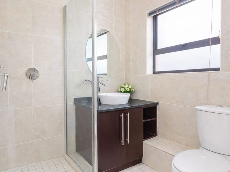 Modern bathroom featuring a glass-enclosed shower, dark wood vanity with granite countertop, vessel sink, and neutral floor-to-ceiling tiling.