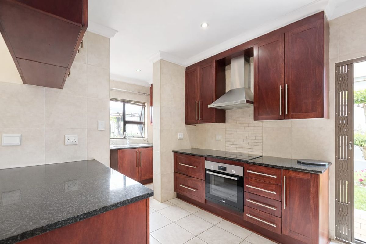 A functional kitchen featuring dark wood cabinetry, granite countertops, built-in oven, and a stainless steel extractor fan, with tiled flooring and backsplash.