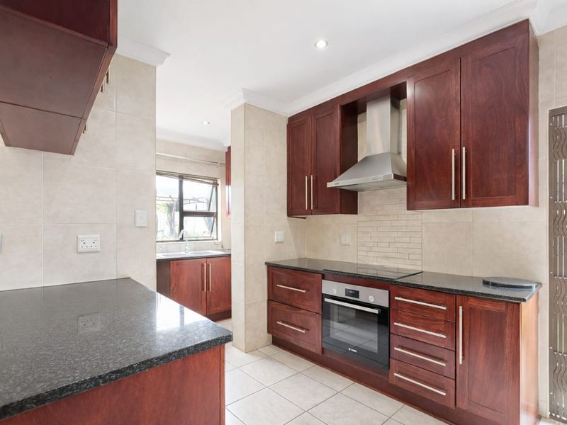 A functional kitchen featuring dark wood cabinetry, granite countertops, built-in oven, and a stainless steel extractor fan, with tiled flooring and backsplash.