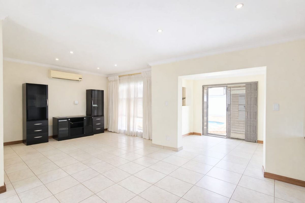 Spacious living area featuring neutral tiled flooring, recessed lighting, and an air conditioning unit, with direct access to the outdoor pool area.