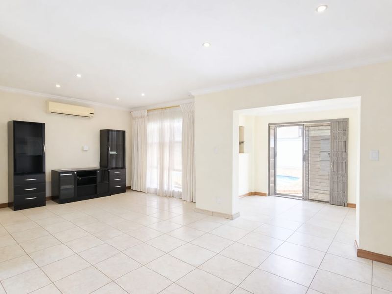 Spacious living area featuring neutral tiled flooring, recessed lighting, and an air conditioning unit, with direct access to the outdoor pool area.