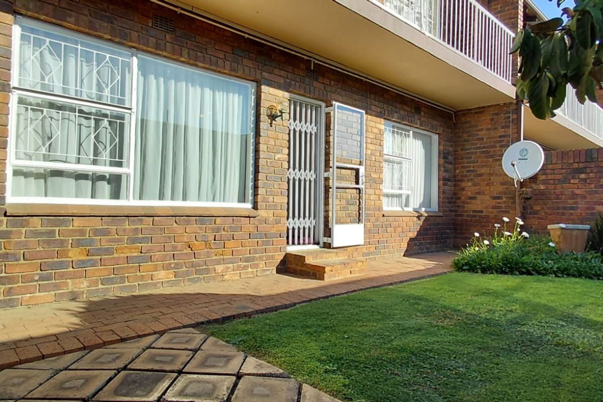 Rear exterior view of the apartment featuring a face brick facade, paved patio area, and a private garden space.
