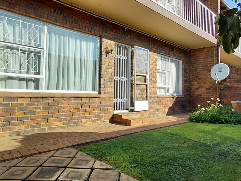 Rear exterior view of the apartment featuring a face brick facade, paved patio area, and a private garden space.