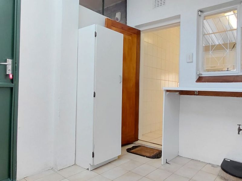 A functional scullery or utility area featuring tiled flooring, built-in cabinetry, and plumbing connections, providing a practical space for laundry or additional kitchen prep.