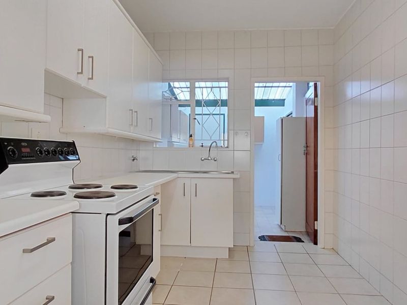 A functional kitchen featuring white built-in cabinetry, a freestanding electric stove, tiled splashbacks, and tiled flooring, with an adjacent utility area.