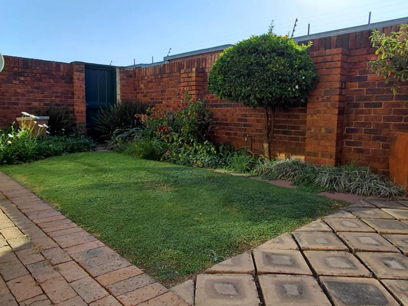 A private rear garden featuring a brick boundary wall, paved patio area, and a small lawn with established garden beds.