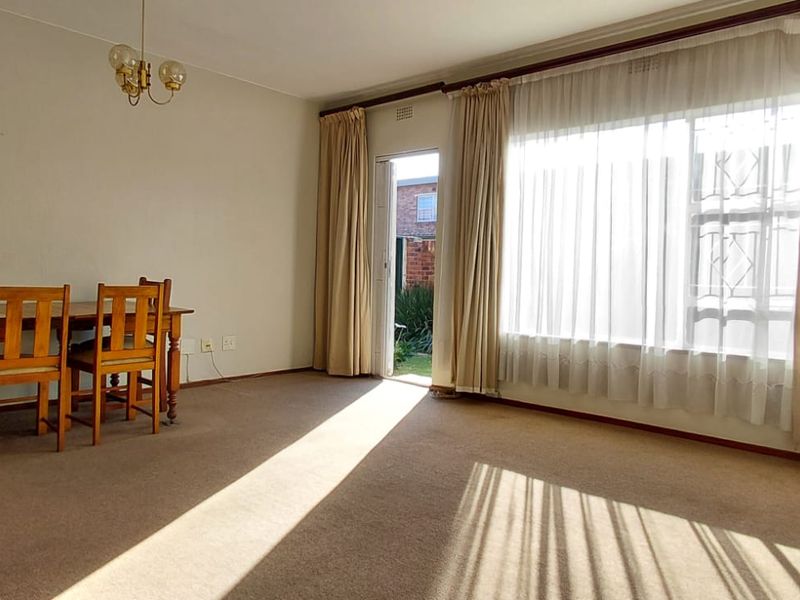 Spacious living area featuring carpet flooring, large windows with natural light, and direct access to the exterior.
