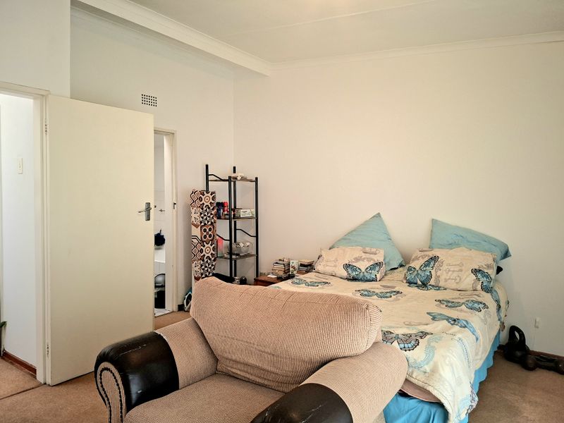 A standard bedroom featuring carpeted flooring, coving, and an adjoining doorway leading to an en-suite or bathroom area.
