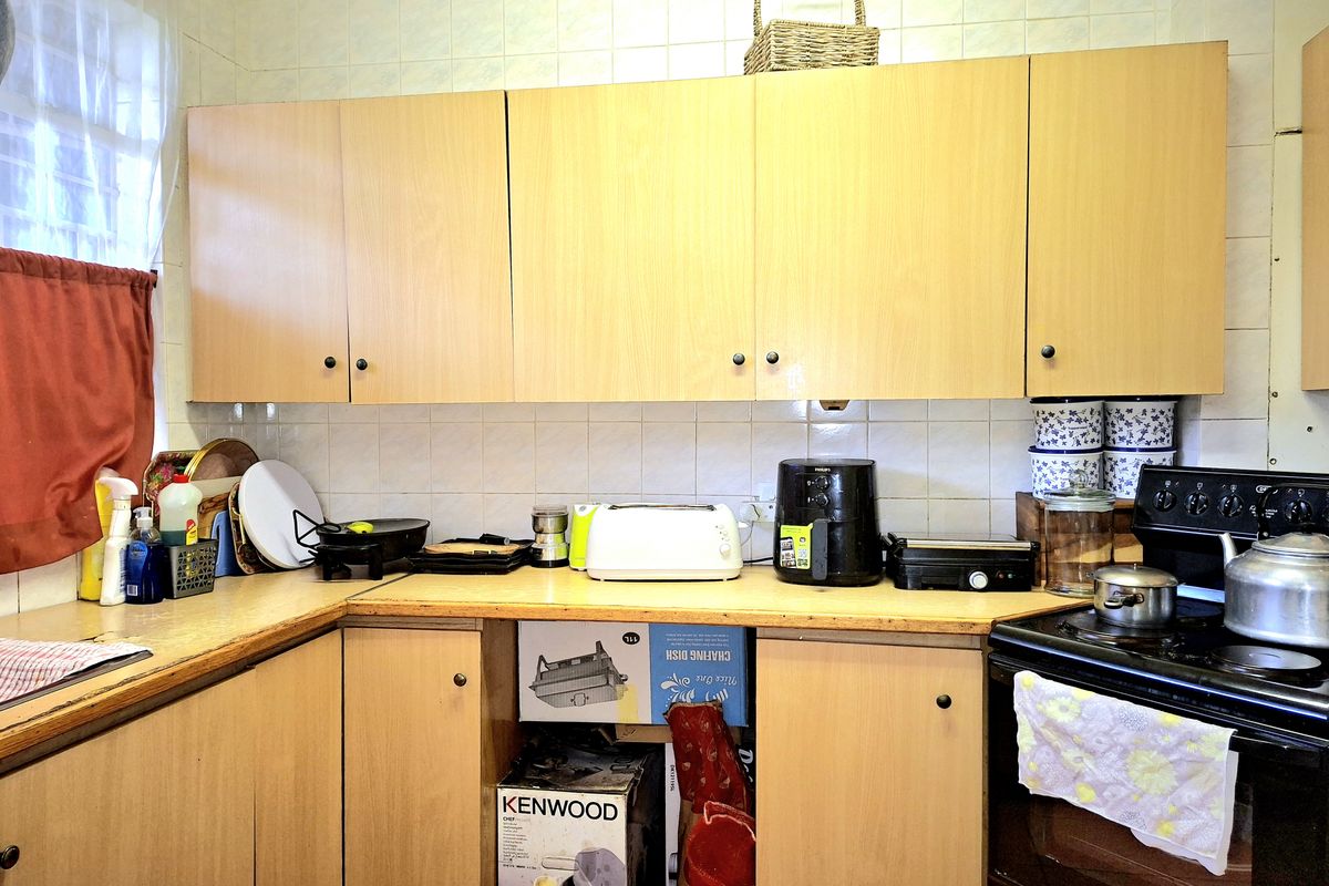 A functional kitchen featuring light wood-tone cabinetry, tiled splashbacks, and a freestanding stove, offering a dated aesthetic ready for modernization.