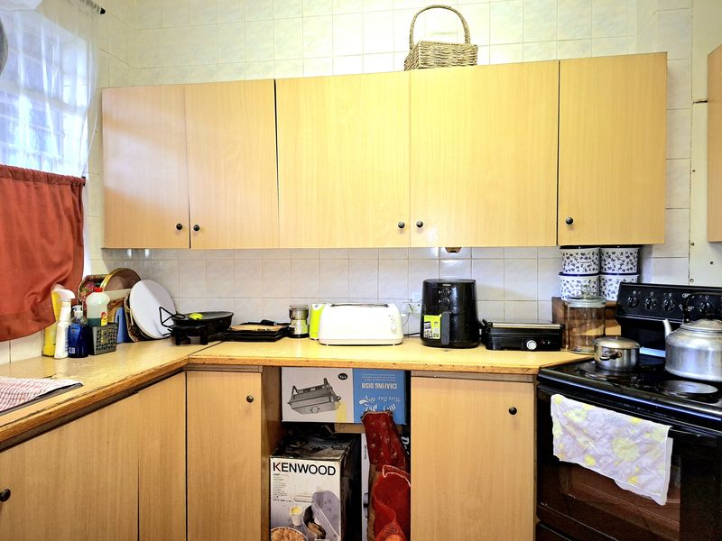 A functional kitchen featuring light wood-tone cabinetry, tiled splashbacks, and a freestanding stove, offering a dated aesthetic ready for modernization.