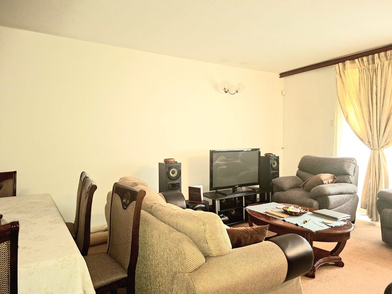 A living room area featuring neutral wall finishes, carpeted flooring, and a window with curtain treatments.