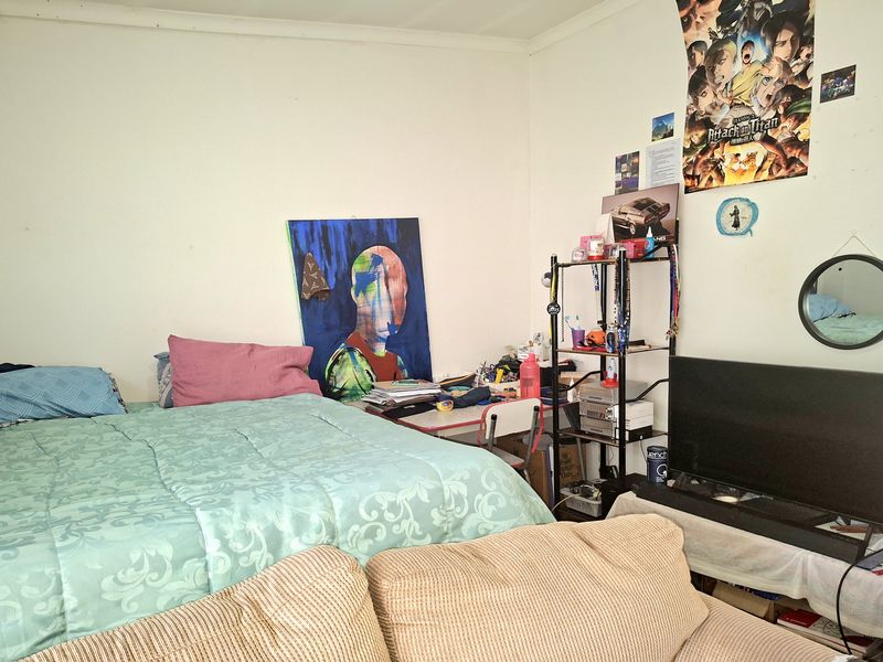 A bedroom space featuring standard wall finishes and flooring, currently utilized as a multi-purpose living and sleeping area.