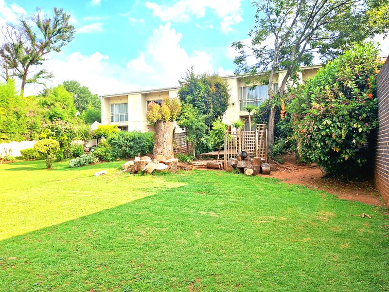 A spacious rear garden featuring a well-maintained lawn, mature trees, and a brick boundary wall, providing a private outdoor space for the townhouse.