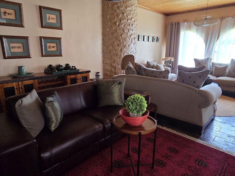 A cozy living room featuring a distinctive stone-clad fireplace, warm timber ceiling, and tiled flooring with large arched windows allowing natural light.