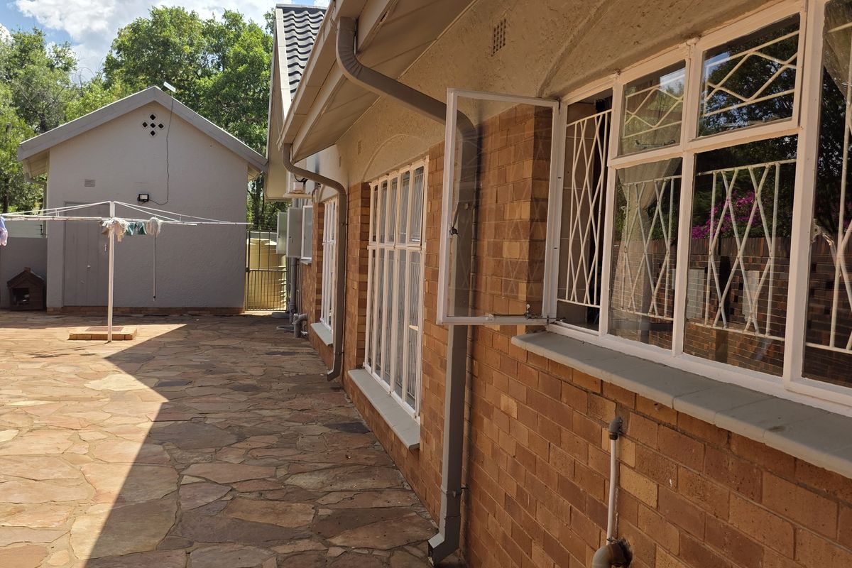 Rear exterior view of the property featuring brick wall construction, stone paved patio area, and security-fitted windows.