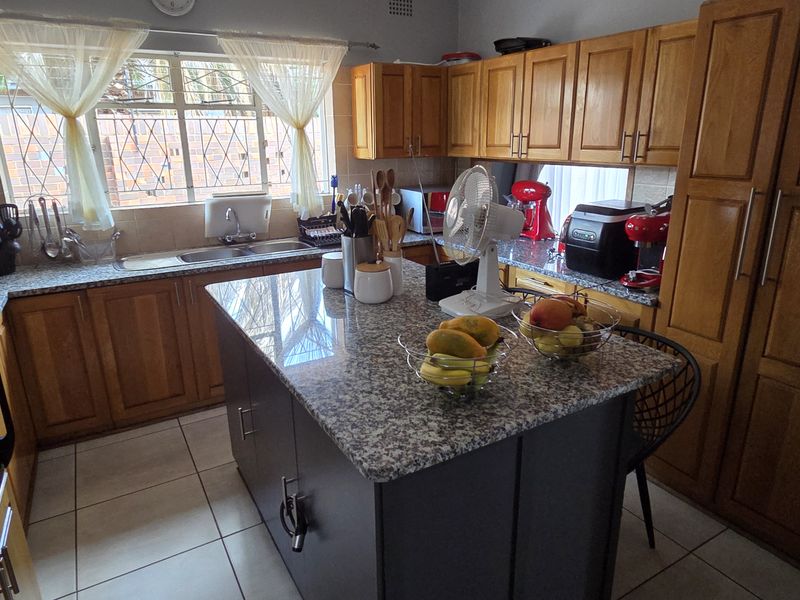 A functional kitchen featuring wooden cabinetry, granite countertops, a central island, and tiled flooring, providing ample workspace and storage.