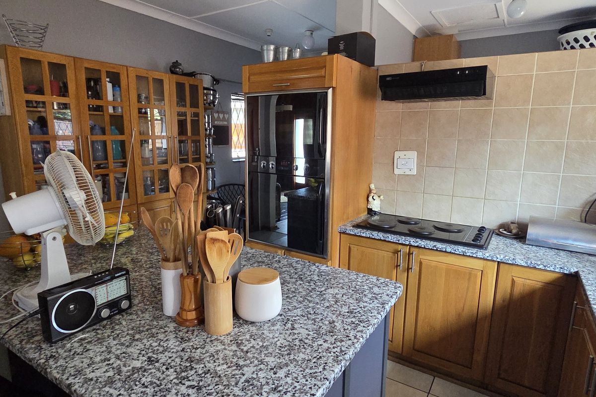 A functional kitchen featuring granite countertops, wooden cabinetry, a built-in oven, and an electric hob with a tiled backsplash.