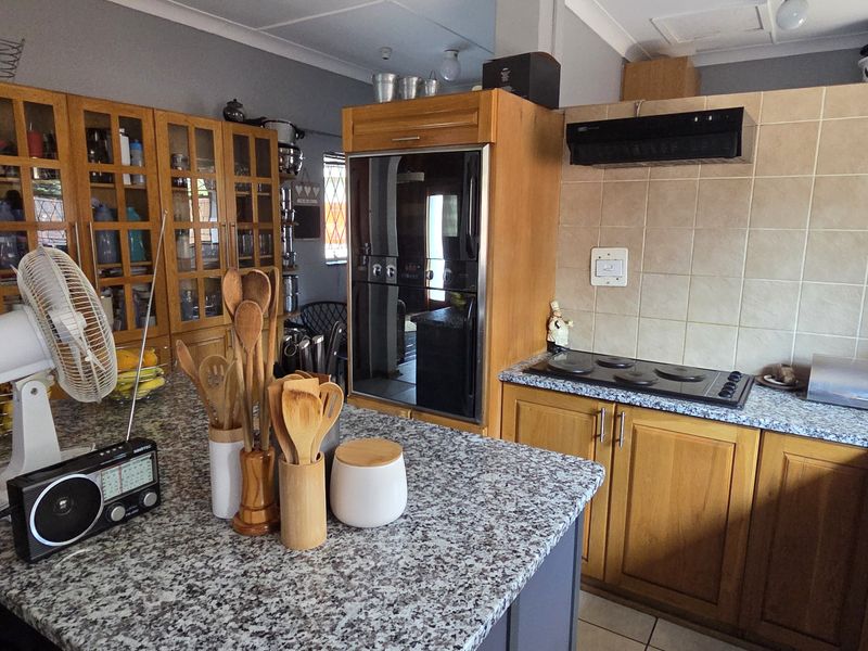 A functional kitchen featuring granite countertops, wooden cabinetry, a built-in oven, and an electric hob with a tiled backsplash.