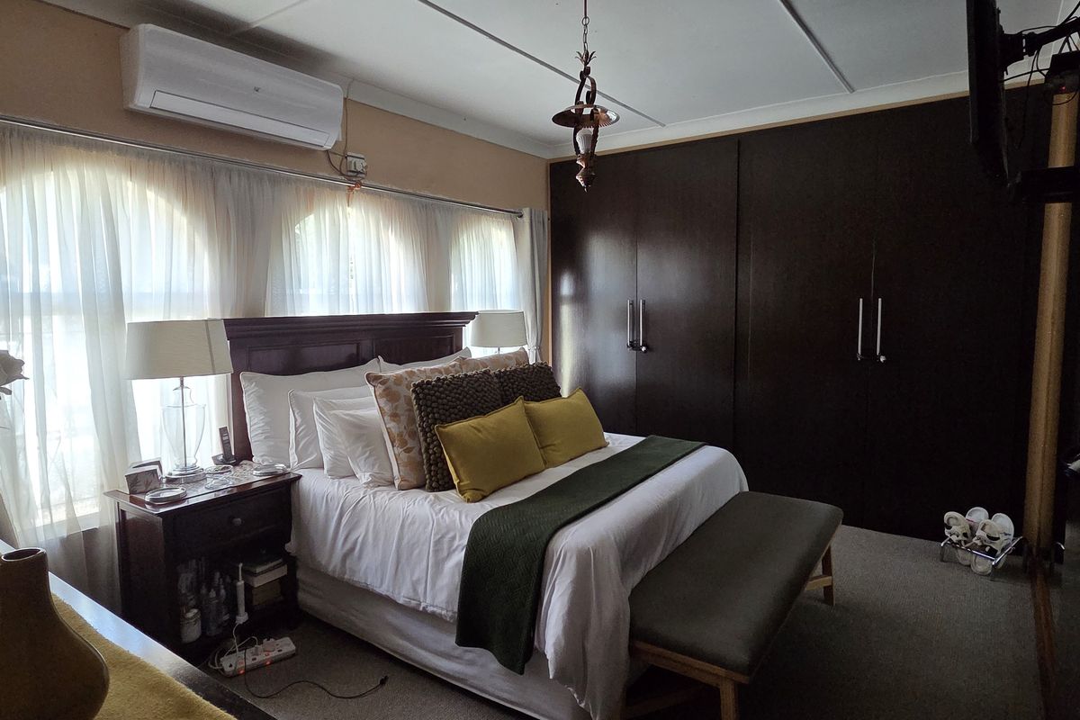 A well-maintained bedroom featuring dark built-in cupboards, carpeted flooring, arched windows, and a wall-mounted split-system air conditioning unit.
