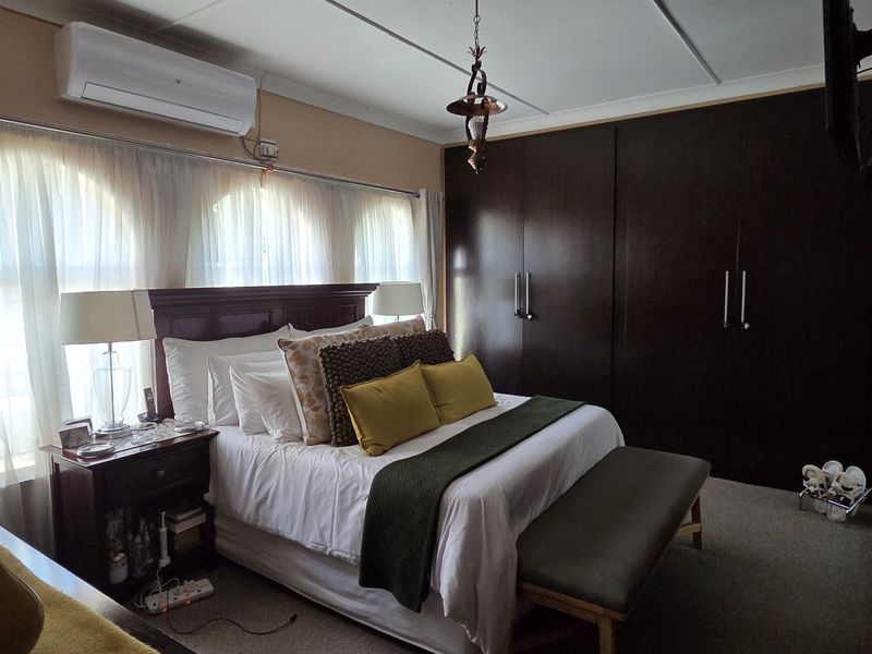 A well-maintained bedroom featuring dark built-in cupboards, carpeted flooring, arched windows, and a wall-mounted split-system air conditioning unit.