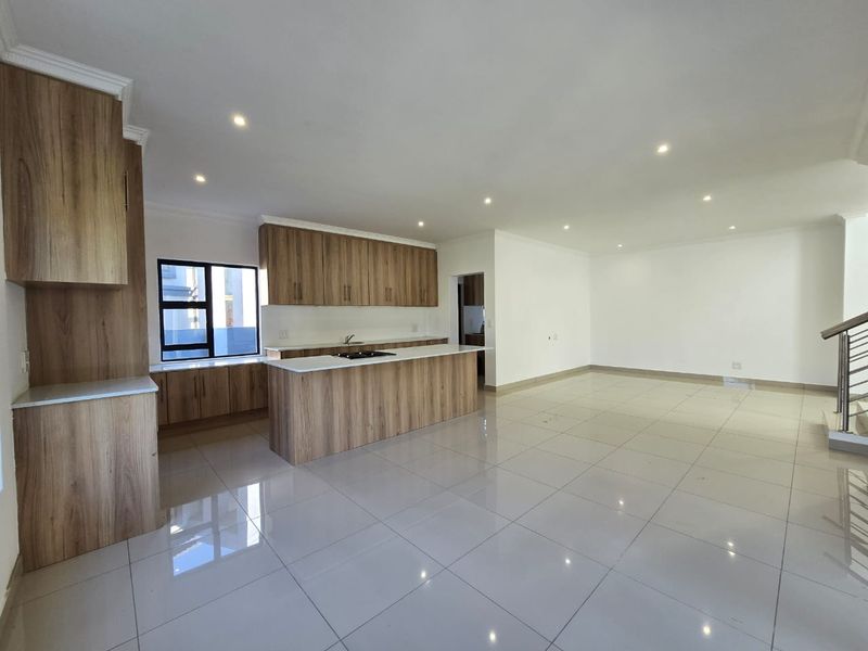 Spacious open-plan living area featuring a modern kitchen with wood-finish cabinetry, a central island with a hob, and polished floor tiles throughout.
