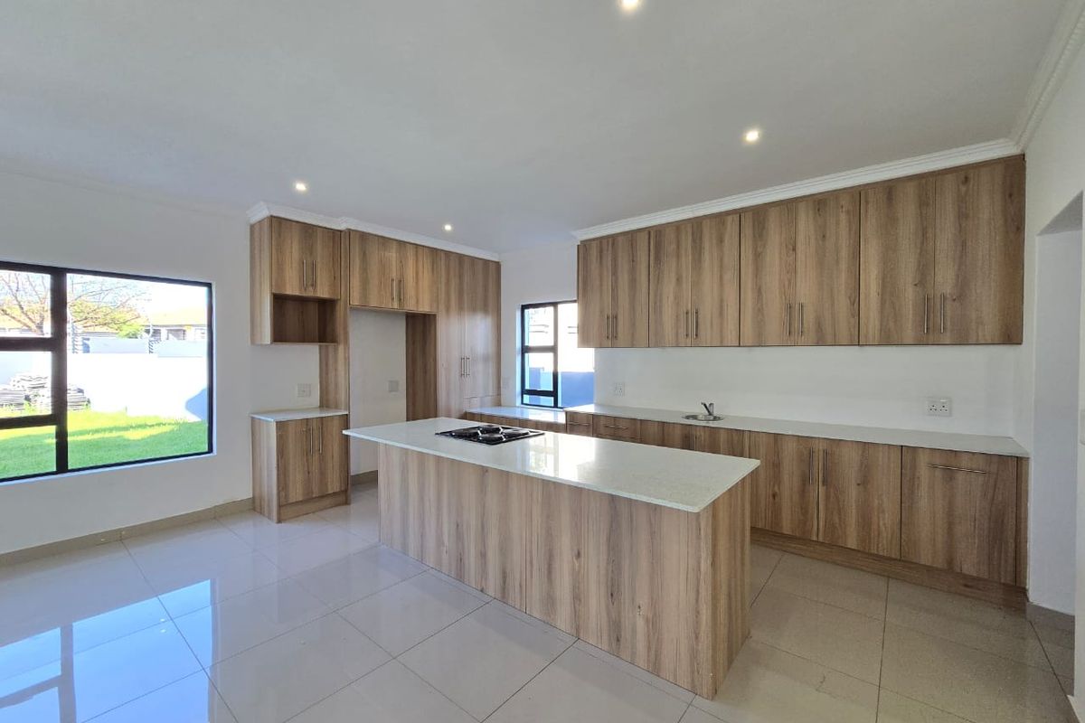 Modern kitchen featuring light wood-grain cabinetry, stone countertops, a central island with a built-in hob, and large windows overlooking the garden.