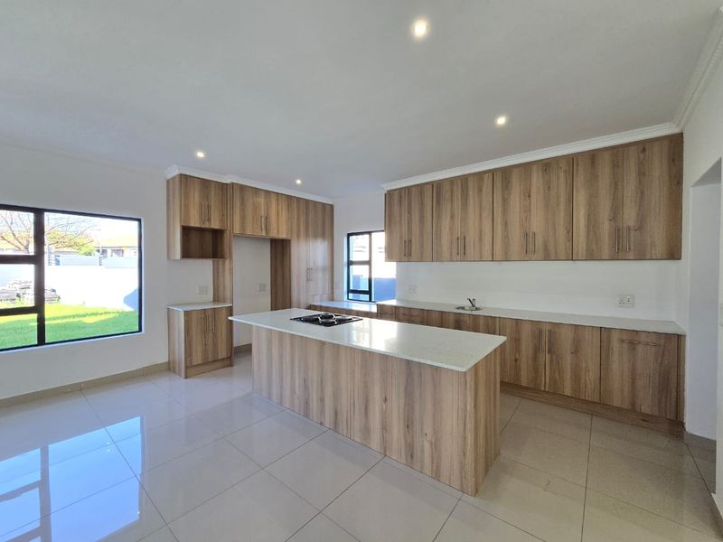 Modern kitchen featuring light wood-grain cabinetry, stone countertops, a central island with a built-in hob, and large windows overlooking the garden.