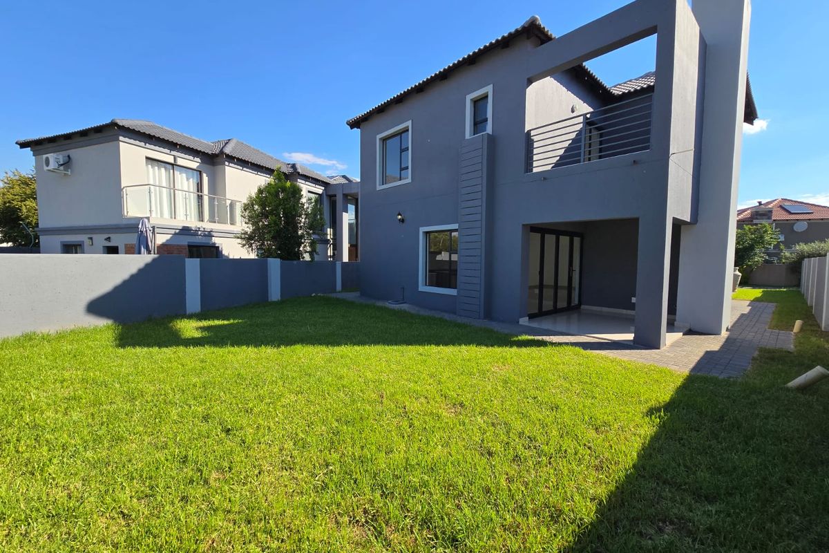 Rear view of a modern two-story house featuring a covered patio, upper-level balcony, and a well-maintained private garden with boundary walling.