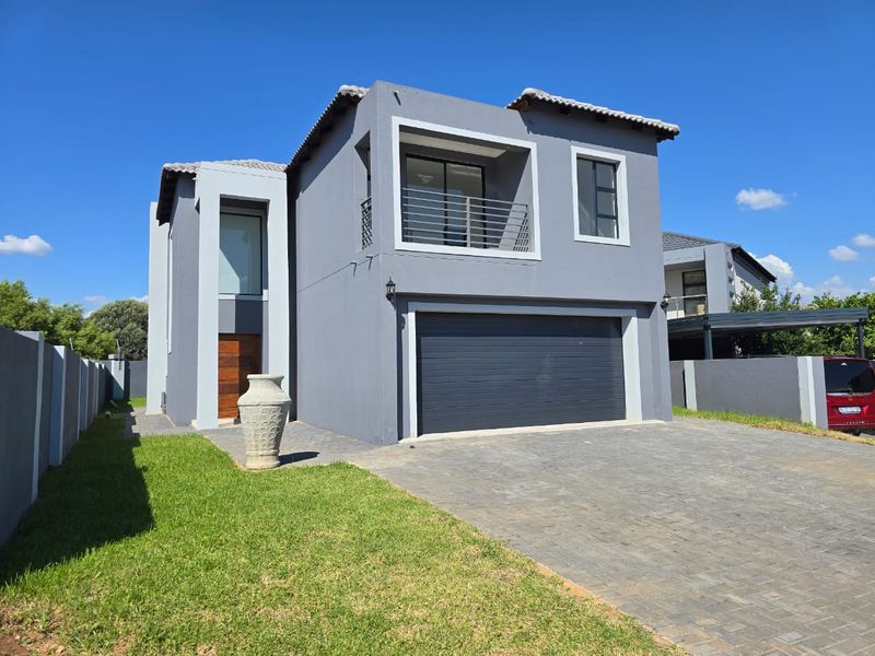 Modern double-storey residential home featuring a double garage, paved driveway, and an upper-level balcony with a contemporary grey facade.