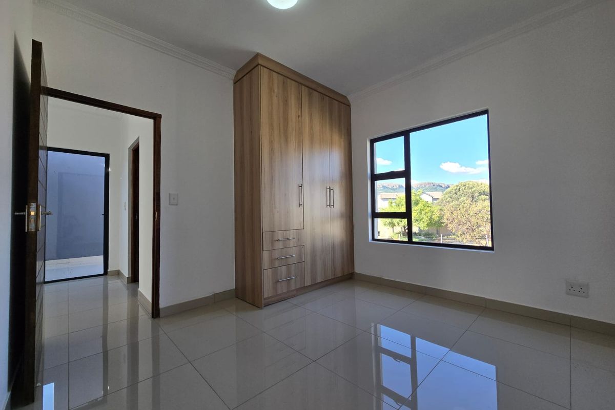 A bright, modern bedroom featuring polished tile flooring, a built-in wooden wardrobe, and large windows providing natural light.