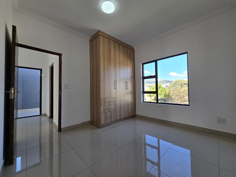 A bright, modern bedroom featuring polished tile flooring, a built-in wooden wardrobe, and large windows providing natural light.
