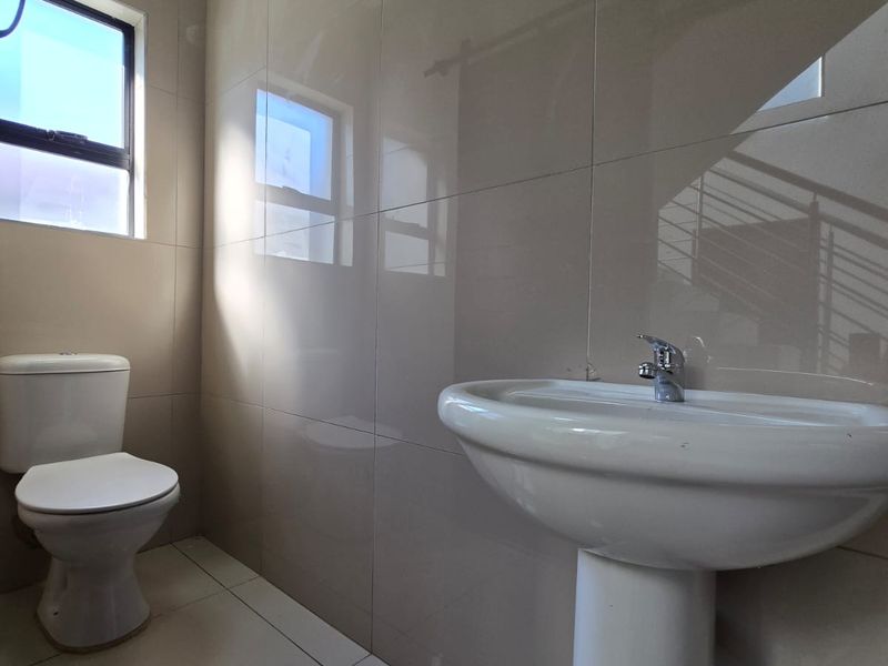A clean, modern bathroom featuring neutral wall and floor tiles, a pedestal washbasin, and a standard toilet.