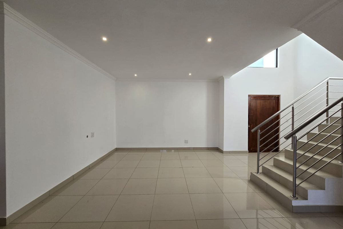 A spacious, open-plan living area featuring neutral tiled flooring, recessed lighting, and a modern staircase with a stainless steel balustrade.
