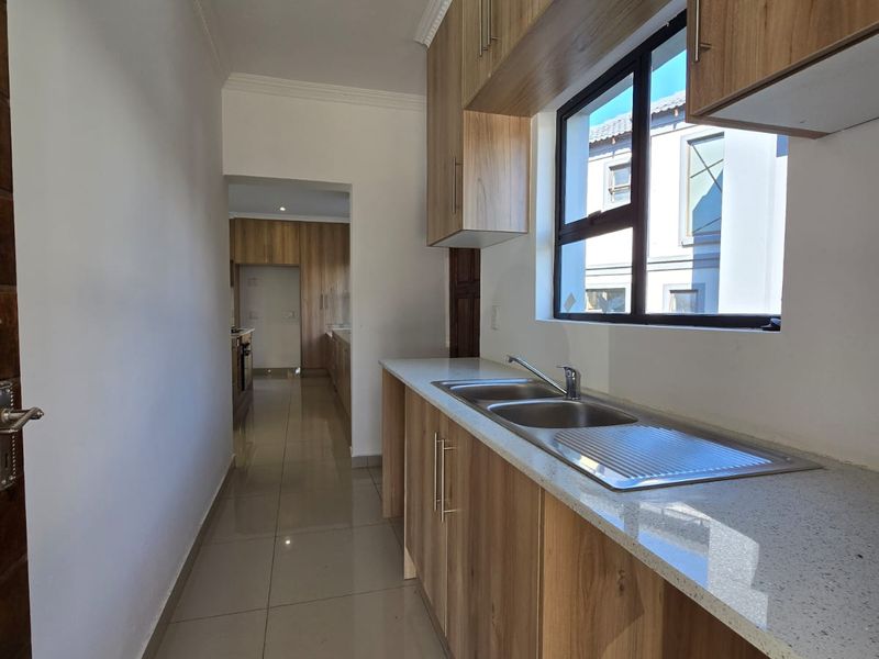 A clean, modern scullery featuring wood-finish cabinetry, stone countertops, a double stainless steel sink, and polished floor tiles.