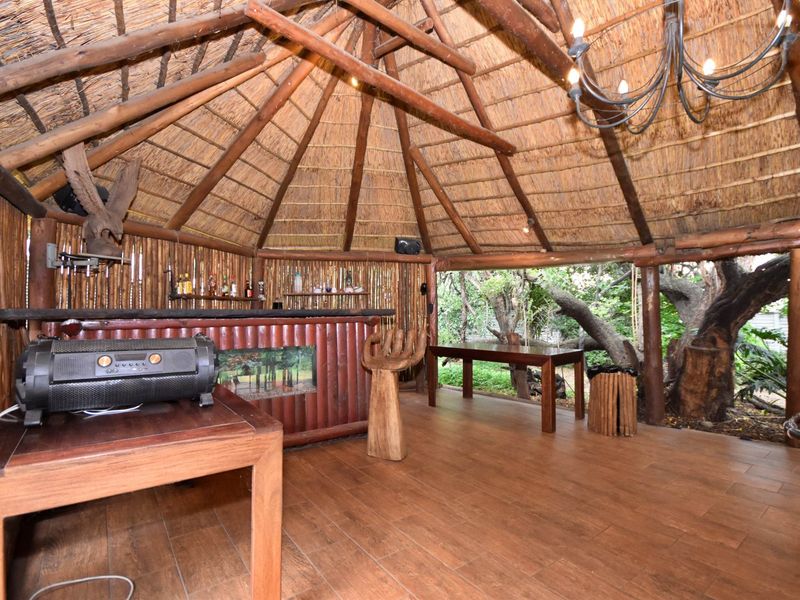 An open-air style bar area featuring a traditional thatched roof, exposed timber rafters, and a built-in bar counter with rustic timber finishes.