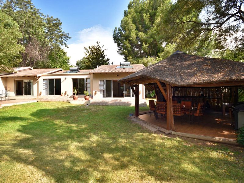 Spacious rear garden featuring a large thatched lapa, paved patio area, and direct access to the home via multiple sliding glass doors.