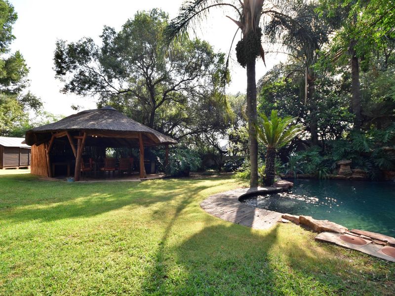 A lush garden setting featuring a swimming pool with a rock water feature and a spacious thatched lapa for outdoor entertaining.