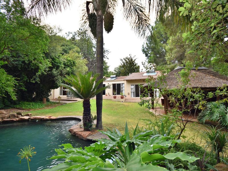 Spacious rear garden featuring a swimming pool, a traditional thatched lapa, and a well-maintained lawn leading to the main residence with solar panels.