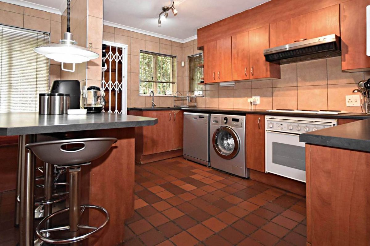Functional kitchen featuring wood-finish cabinetry, tiled flooring, integrated appliance spaces, and a breakfast counter, offering a practical layout for daily meal preparation.