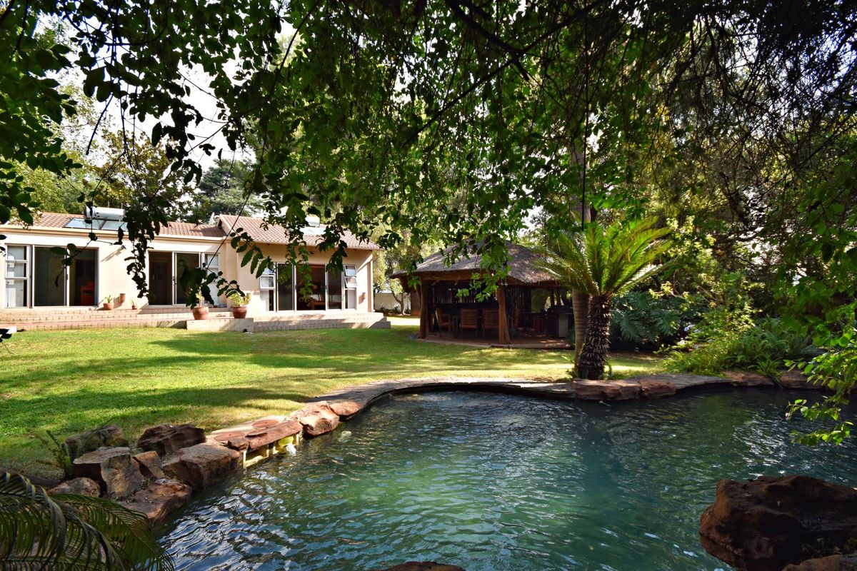 Rear garden view featuring a swimming pool with natural rock edging, a thatched gazebo, and a paved patio area leading to the main house.