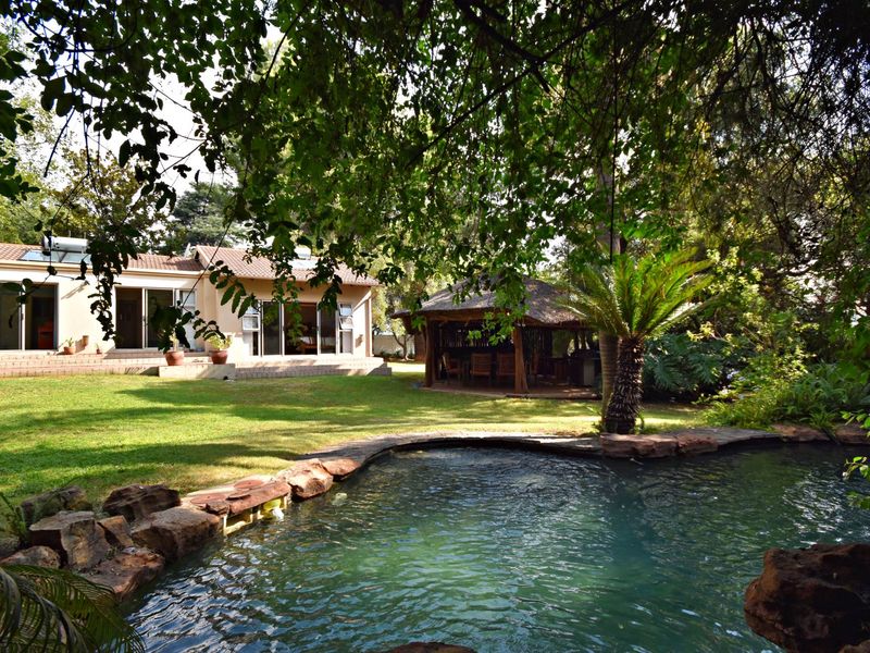Rear garden view featuring a swimming pool with natural rock edging, a thatched gazebo, and a paved patio area leading to the main house.