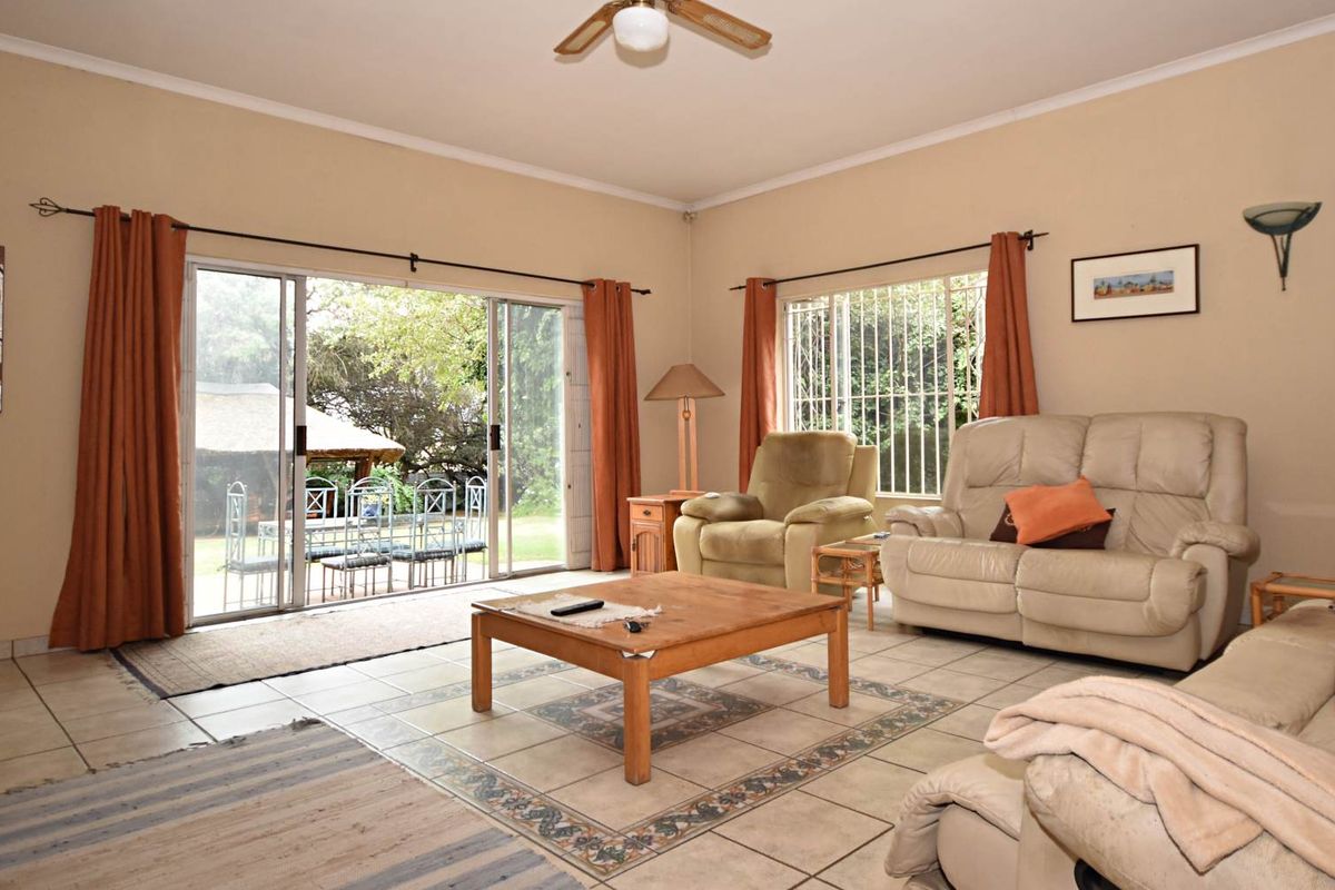 Spacious living room featuring tiled flooring, a ceiling fan, and large sliding glass doors providing direct access to the outdoor patio and garden area.