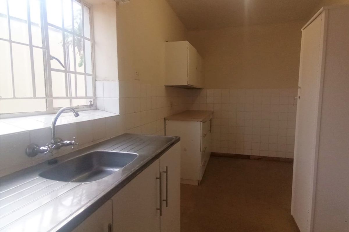 A functional, empty kitchen featuring built-in cabinetry, a stainless steel sink, and tiled splashbacks, offering a blank canvas for renovation.